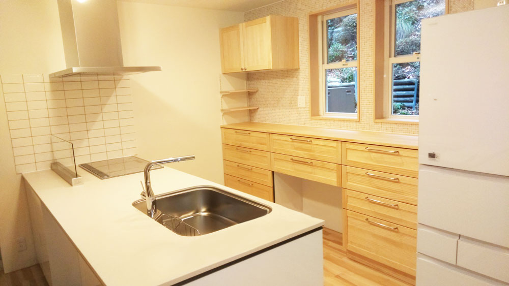 白色のキッチン、無垢材のカップボード、キッチン背面の壁はモザイクタイルにし、全体的に温かみのある空間に。